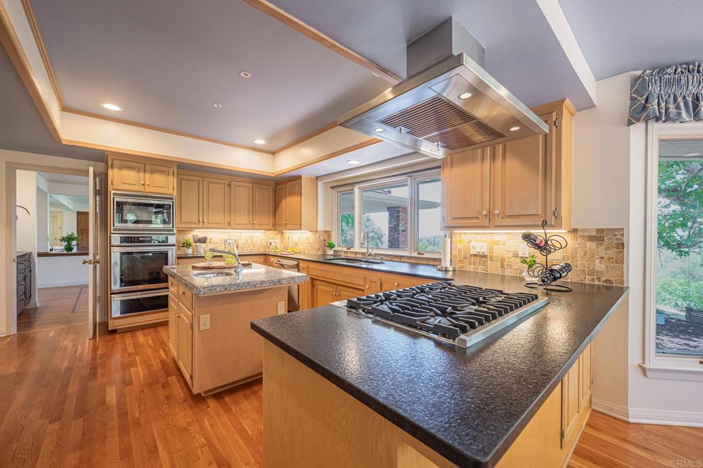145 Yucca Road Fallbrook, CA 92028 - Photo 14 of 58 a kitchen with stainless steel appliances granite countertop a stove top oven a sink dishwasher a dining table and chairs with wooden floor