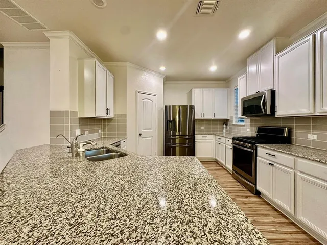 a kitchen with stainless steel appliances granite countertop a stove a sink a refrigerator white cabinets and a granite counter top