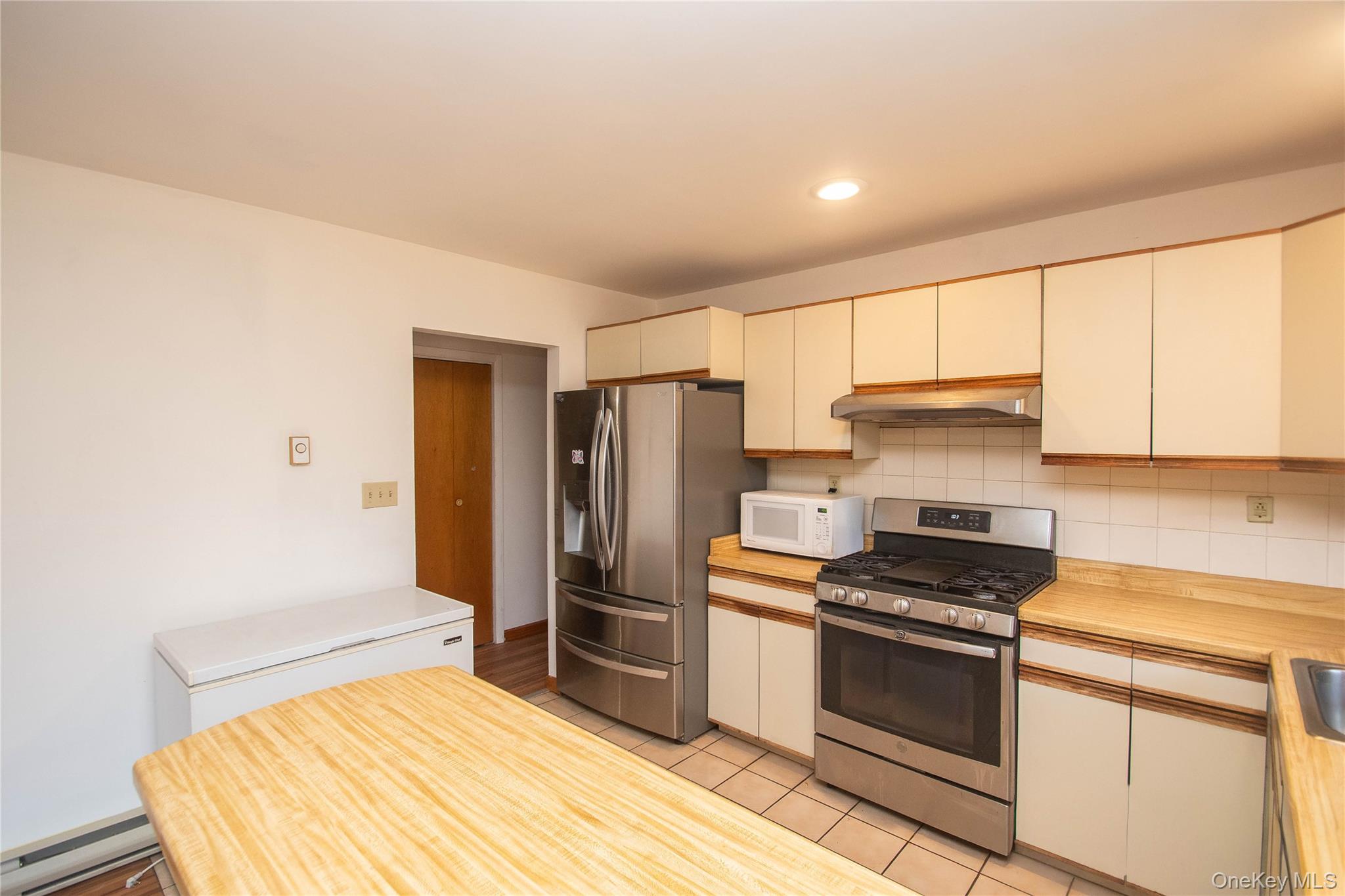 20 Valley Road Forestburgh, NY 12777 - Photo 11 of 38 Kitchen with stainless steel appliances, decorative backsplash, light tile patterned flooring, a baseboard radiator, and under cabinet range hood