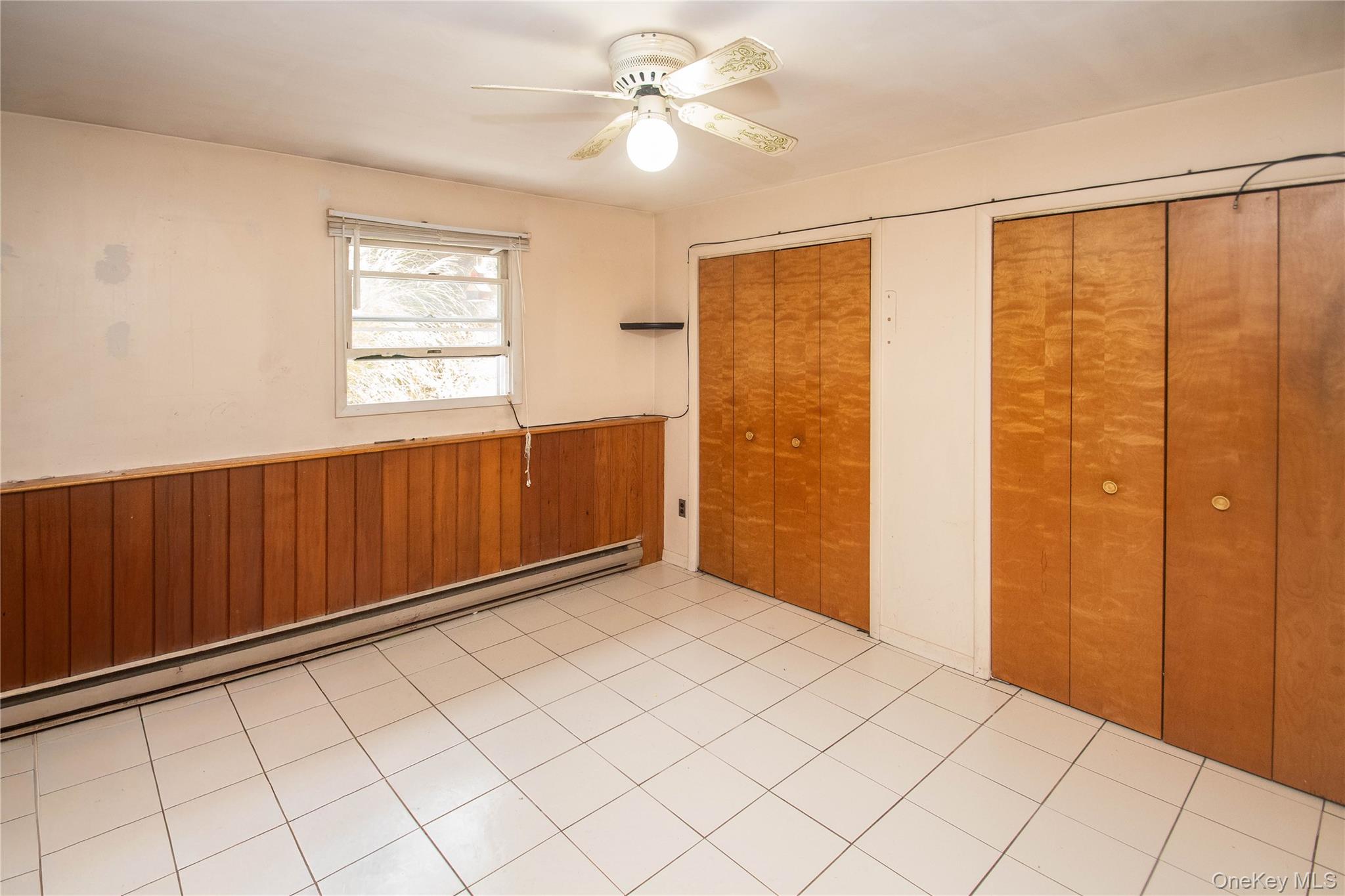 20 Valley Road Forestburgh, NY 12777 - Photo 28 of 38 Unfurnished bedroom with wainscoting, wooden walls, a baseboard heating unit, two closets, and a ceiling fan