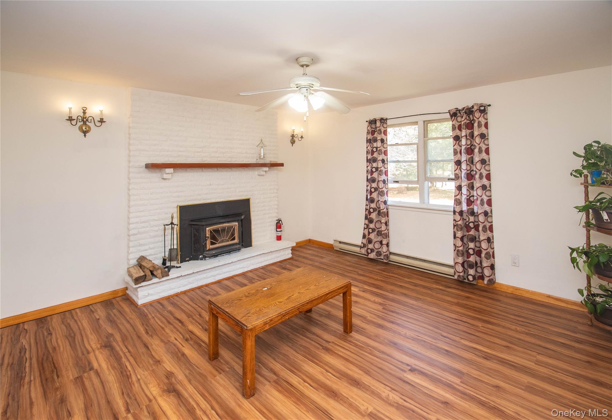 20 Valley Road Forestburgh, NY 12777 - Photo 5 of 38 Living area featuring wood finished floors, ceiling fan, a baseboard heating unit, and a wood stove