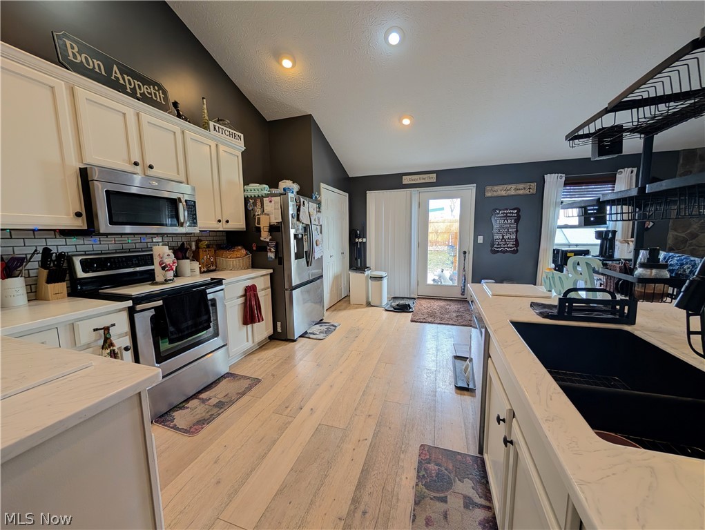 7360 Jones Road Nashport, OH 43830 - Photo 13 of 29 Kitchen featuring stainless steel appliances, decorative backsplash, vaulted ceiling, light wood-style flooring, and white cabinets