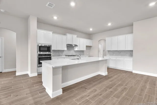 a large kitchen with kitchen island a sink wooden floor and stainless steel appliances