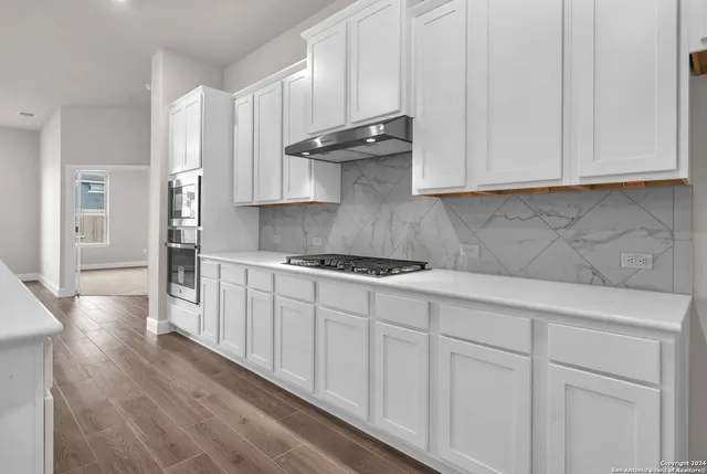 a kitchen with stainless steel appliances granite countertop white cabinets and a stove top oven