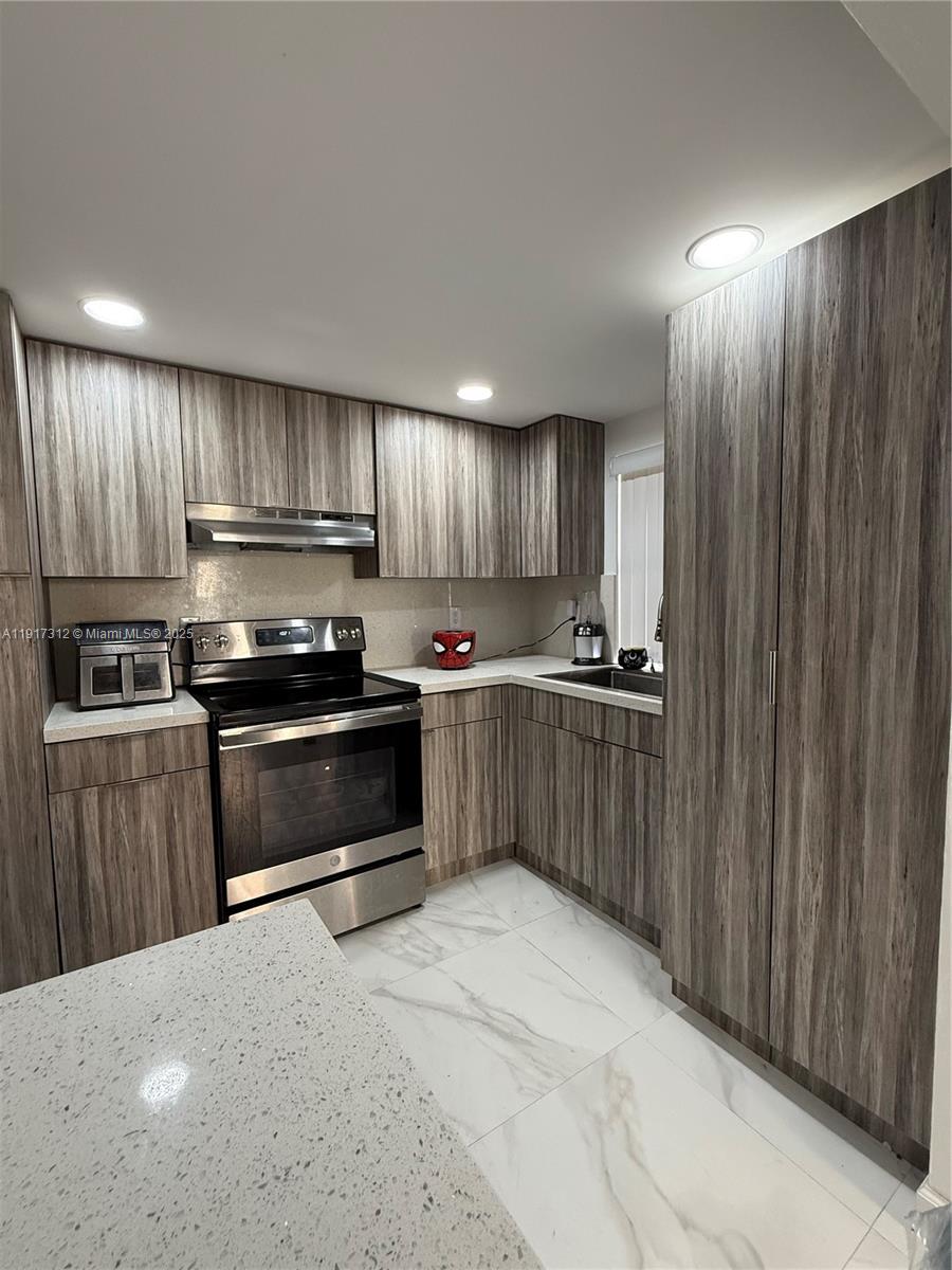 4850 Southwest 63rd Terrace, Unit 312 Davie, FL 33314 - Photo 2 of 27 a kitchen with kitchen island granite countertop wooden cabinets and stainless steel appliances