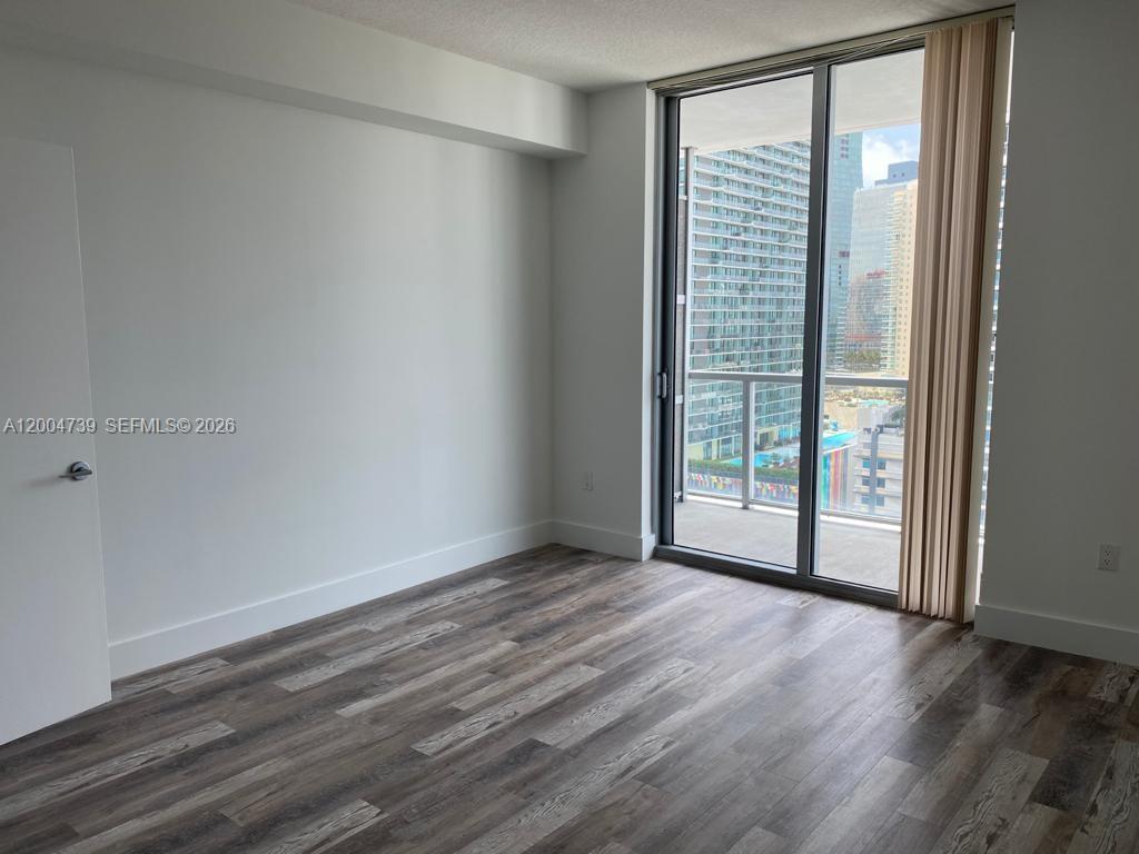 79 Southwest 12th Street, Unit 2403S Miami, FL 33130 - Photo 10 of 12 a view of an empty room with wooden floor and a window