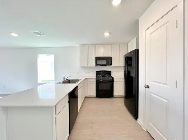 a kitchen with a refrigerator a sink a stove top oven and white cabinets