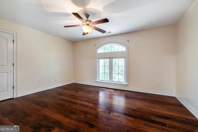 an empty room with wooden floor chandelier fan and windows