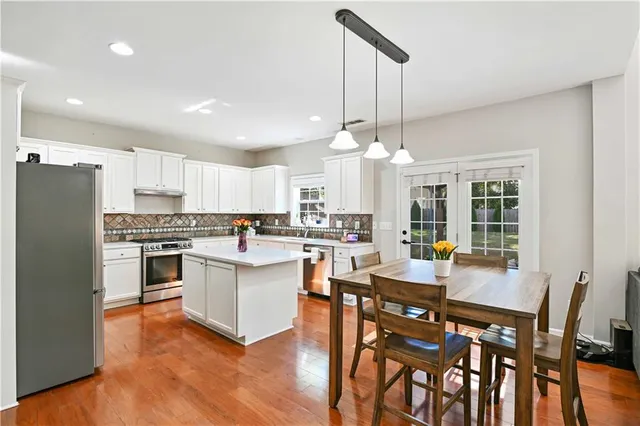 a open kitchen with stainless steel appliances granite countertop a stove a refrigerator a kitchen island a dining table and chairs with wooden floor
