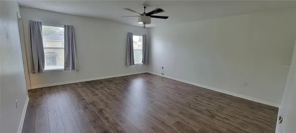 an empty room with wooden floor chandelier fan and windows