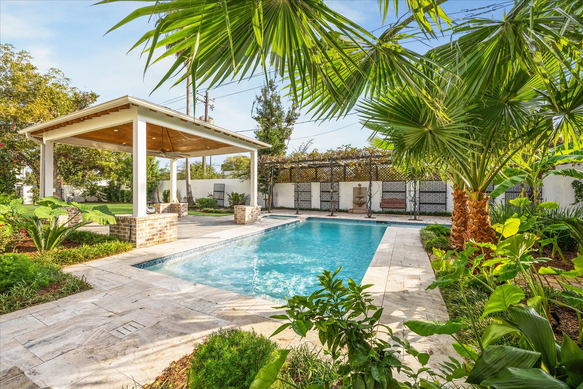 607 Harvard Street Houston, TX 77007 - Photo 4 of 50 Built in 2021, the exquisite outdoor entertaining spaces feature a heated swimming pool, spa, a large dining pavilion, a beautiful pergola, and a beautifully equipped outdoor kitchen, all surrounded by palms and climbing vines.