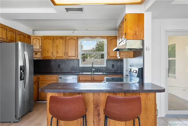 a kitchen with stainless steel appliances granite countertop a table chairs sink and window