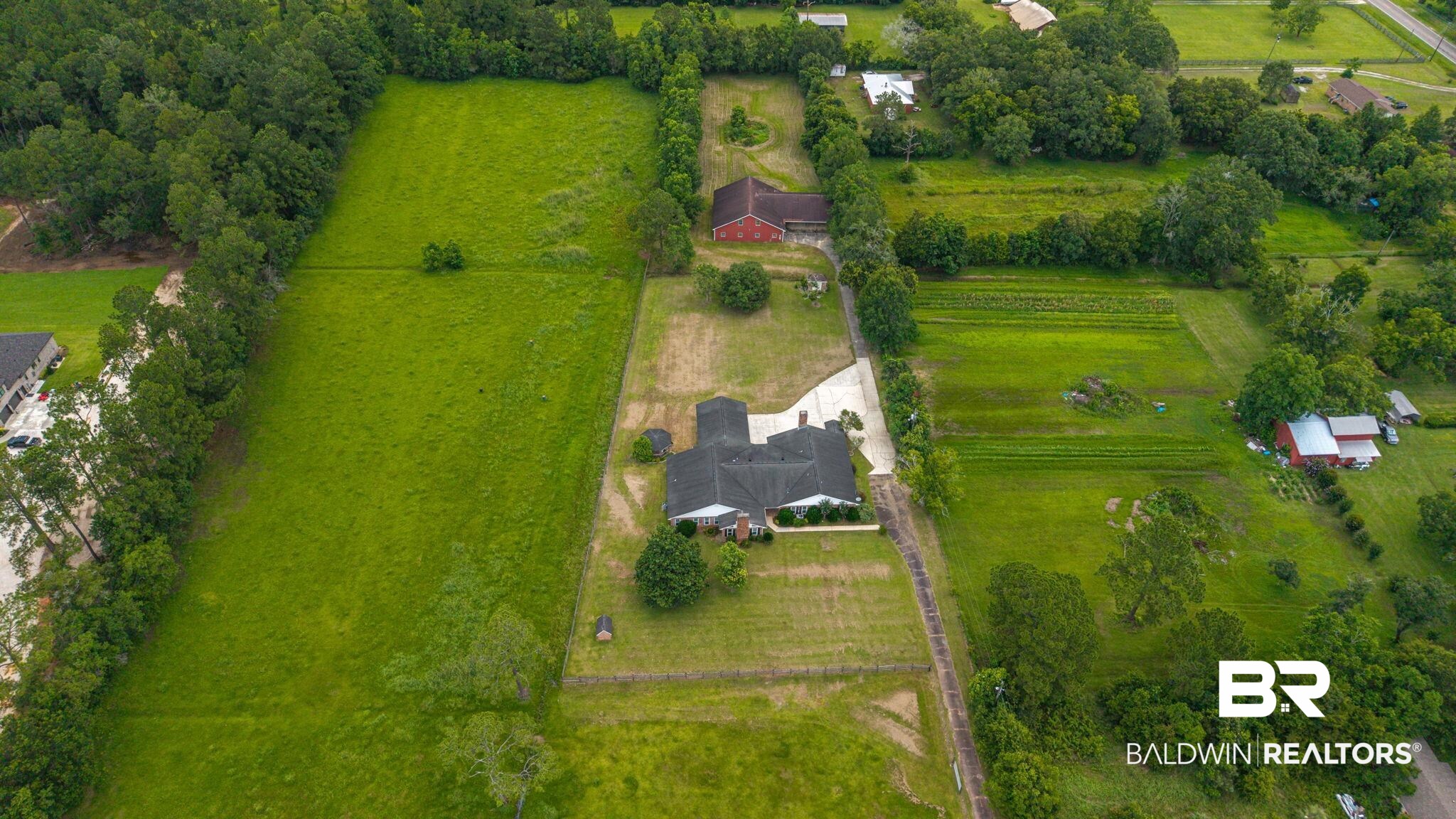 7540 2 Mile Road Irvington, AL 36544 - Photo 77 of 82 Expansive property featuring a single-story residence with a dark shingle roof, a red brick building, and multiple cultivated green fields