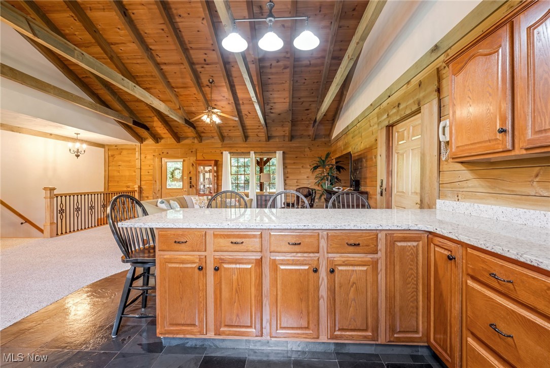 1623 Carson Road New Cumberland, WV 26047 - Photo 11 of 40 Kitchen featuring a kitchen breakfast bar, wood walls, ceiling fan with notable chandelier, dark carpet, and wood ceiling