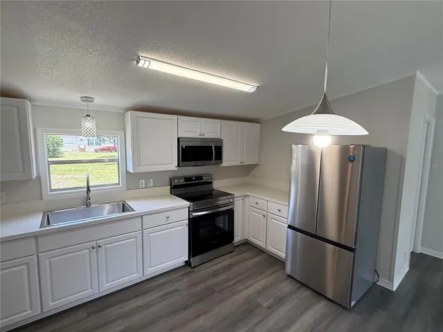 a kitchen with stainless steel appliances granite countertop a refrigerator a sink dishwasher a oven with white cabinets and wooden floor