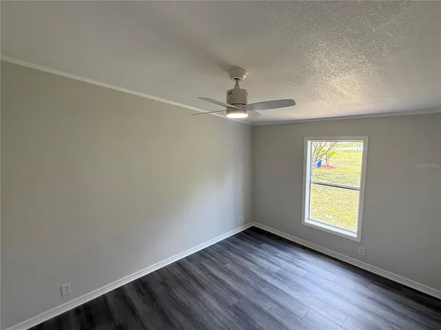 an empty room with wooden floor chandelier fan and windows