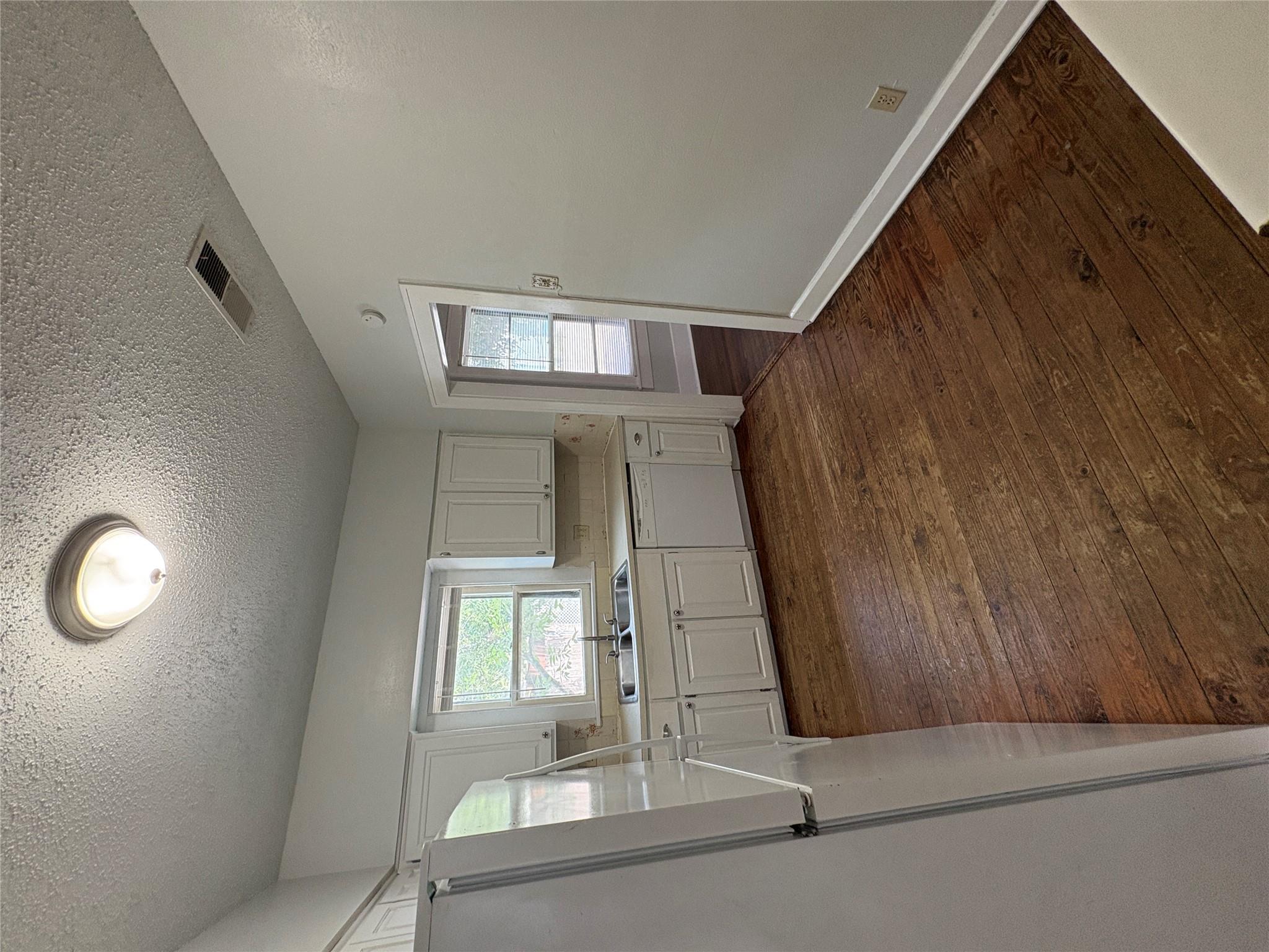 915 West 29th Street Austin, TX 78705 - Photo 13 of 20 Kitchen featuring wood-finish flooring, white cabinetry, a double basin stainless steel sink, and a white dishwasher