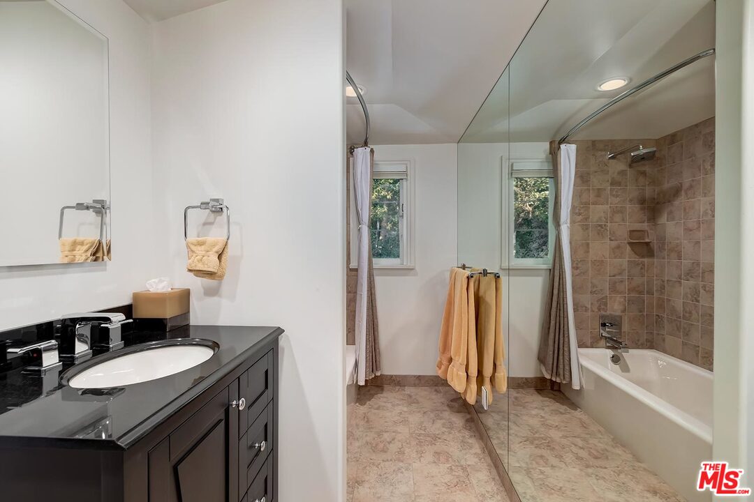 1130 Tower Road Beverly Hills, CA 90210 - Photo 23 of 30 a bathroom with a granite countertop sink a mirror a bathtub and shower