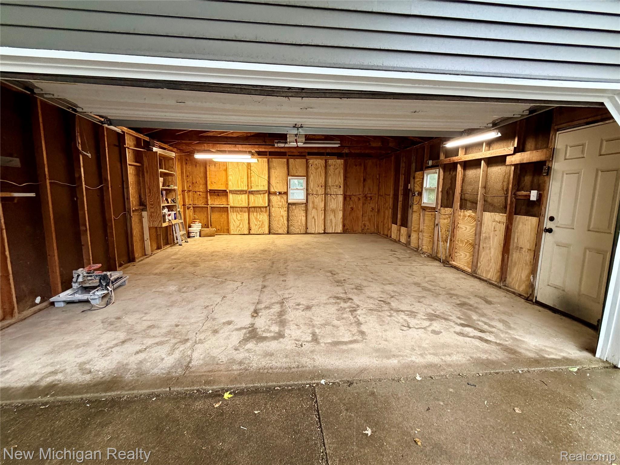 7104 Willard Road Millington, MI 48746 - Photo 23 of 30 Spacious interior garage featuring exposed wood framing, concrete flooring, and ceiling-mounted fluorescent lighting