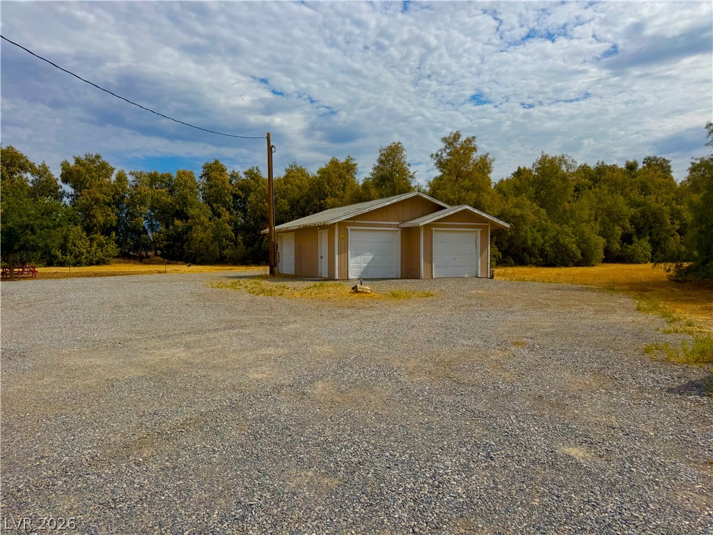 Two-car detached garage with ample gravel parking offers practical utility amidst natural surroundings.