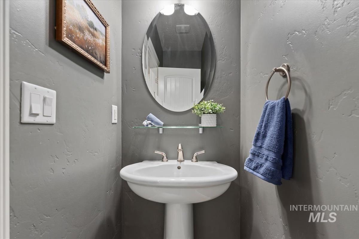 640 Southwest Miner Street Mountain Home, ID 83647 - Photo 14 of 35 Pedestal sink with brushed nickel faucet, oval mirror, wall-mounted light fixture, and textured gray walls