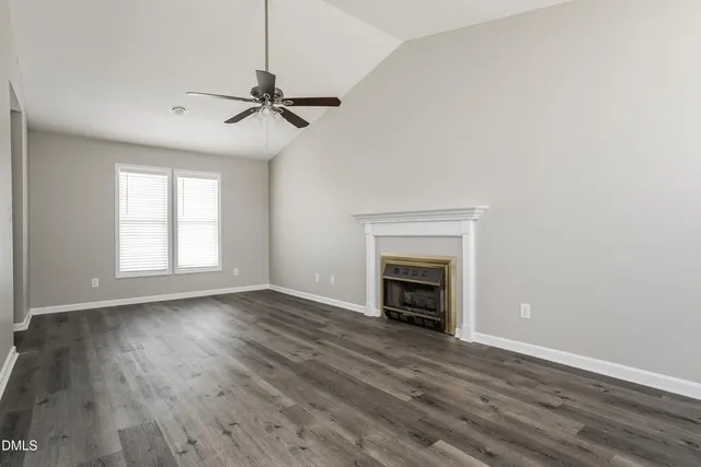 an empty room with wooden floor fireplace and windows