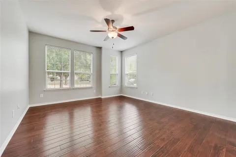 an empty room with wooden floor fan and windows