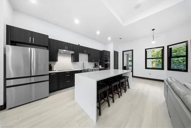 a kitchen with stainless steel appliances kitchen island granite countertop a refrigerator a sink dishwasher a dining table and chairs with wooden floor