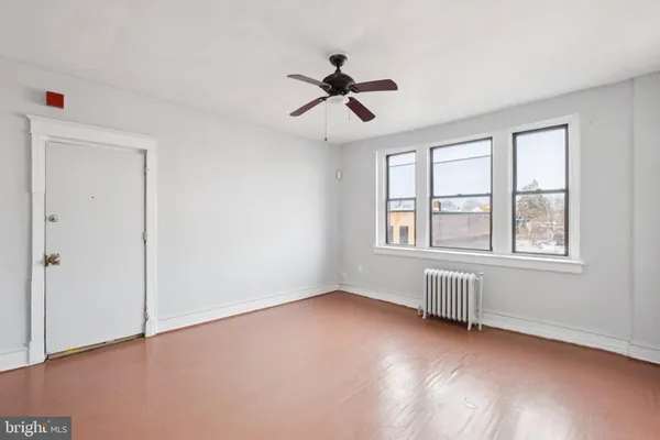 a view of an empty room with wooden floor and a ceiling fan