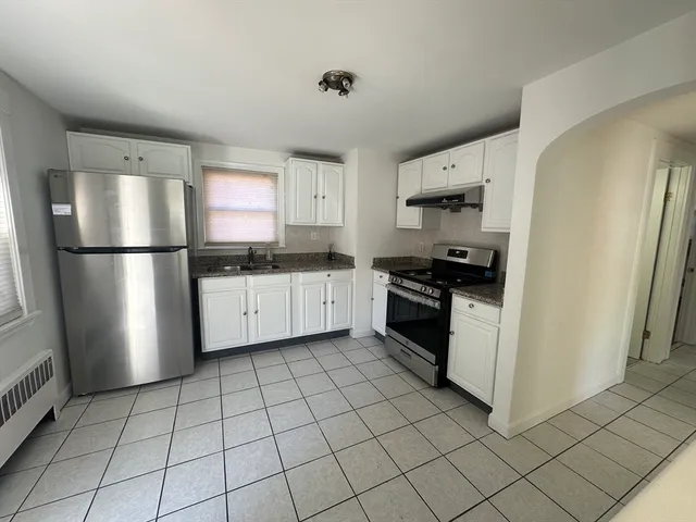 a kitchen with white cabinets a sink a stove a refrigerator and a window