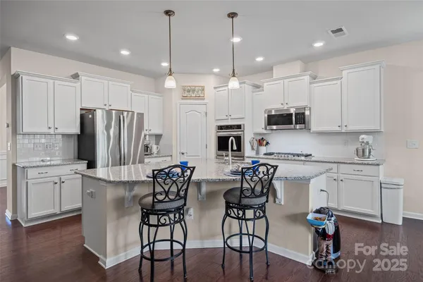 a kitchen with stainless steel appliances kitchen island granite countertop a dining table chairs refrigerator and sink