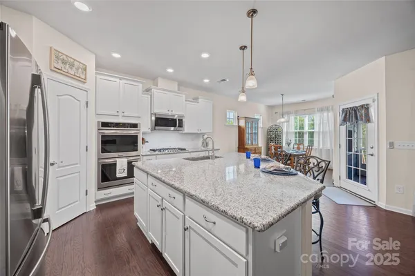 a kitchen with stainless steel appliances granite countertop a kitchen island a stove a refrigerator a oven and a sink with wooden floor