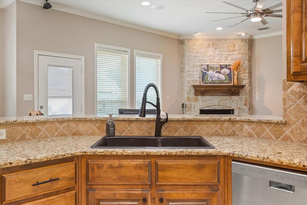 203 Silver Spur Trail Waco, TX 76657 - Photo 12 of 39 Kitchen with dishwasher, decorative backsplash, ornamental molding, light stone counters, and brown cabinetry