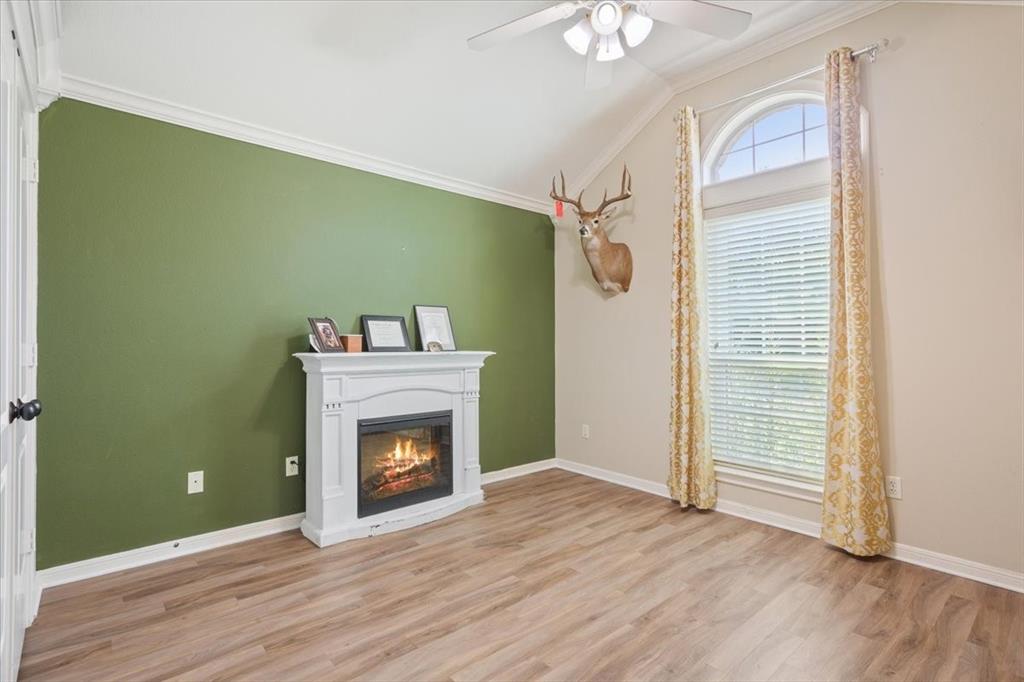 203 Silver Spur Trail Waco, TX 76657 - Photo 22 of 39 Living room featuring crown molding, a glass covered fireplace, light wood-type flooring, lofted ceiling, and a ceiling fan