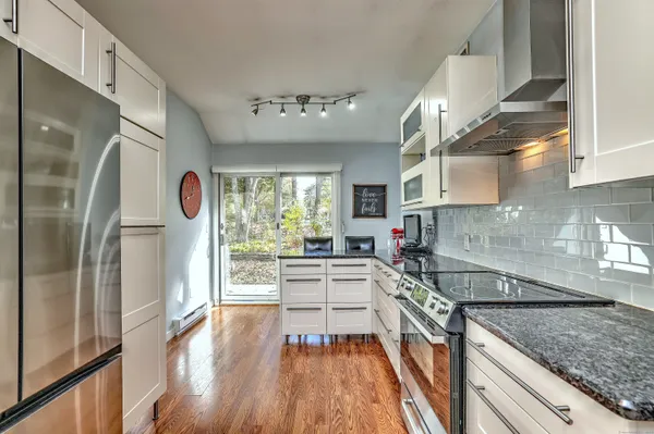 a kitchen with stainless steel appliances granite countertop a refrigerator a sink dishwasher a stove and white countertops with wooden floor