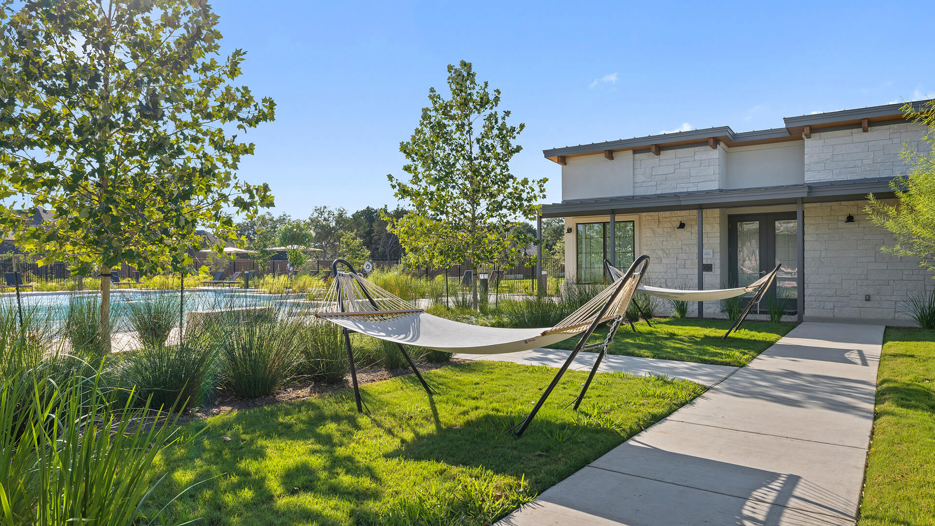 Concrete walkways cross manicured lawns leading to a contemporary stone facade under blue skies.
