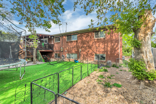 7470 Ramanee Drive Midvale, UT 84047 - Photo 27 of 29 Back of house with a trampoline, a fenced backyard, a deck, a gate, and brick siding