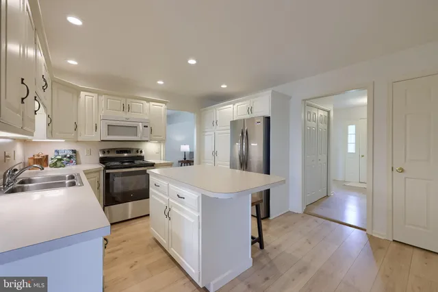 a kitchen with stainless steel appliances kitchen island a sink dishwasher a refrigerator and a stove with wooden floor