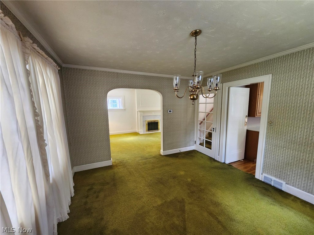 Unfurnished dining area with a chandelier, ornamental molding, and dark colored carpet