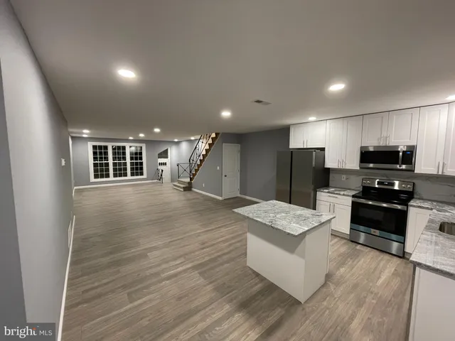 a large kitchen with stainless steel appliances granite countertop a stove a sink a refrigerator white cabinets and wooden floor