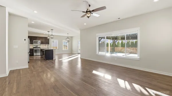 a view of a kitchen and an empty room with wooden floor and a kitchen