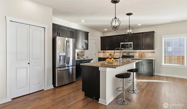 a kitchen with stainless steel appliances granite countertop a refrigerator a stove top oven a sink dishwasher a dining table and chairs with wooden floor