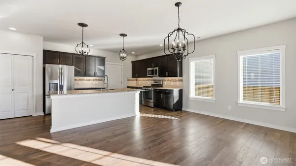 a view of a kitchen with stainless steel appliances granite countertop a refrigerator a microwave a stove and white cabinets with wooden floor