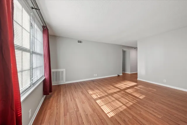 a view of an empty room with wooden floor and a window