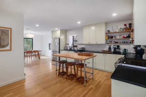 a kitchen with stainless steel appliances granite countertop a stove top oven a sink a dining table and chairs with wooden floor