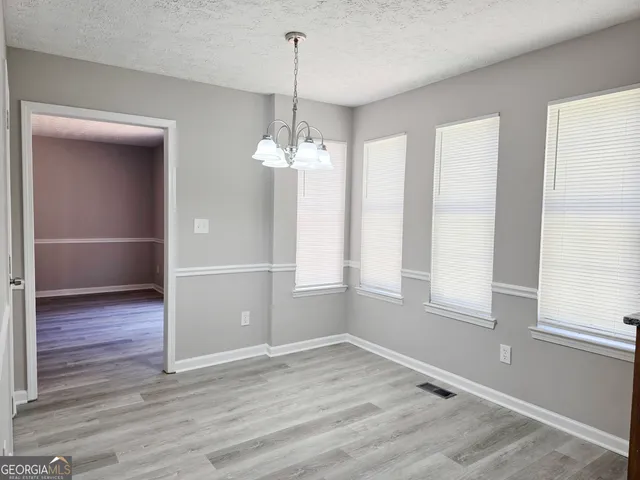 an empty room with wooden floor chandelier and windows
