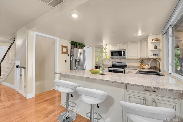 a kitchen with stainless steel appliances granite countertop a refrigerator a stove a sink dishwasher and white cabinets with wooden floor