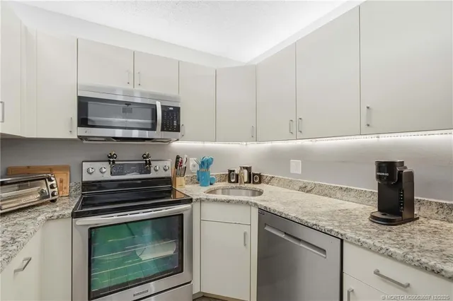a kitchen with granite countertop white cabinets white stainless steel appliances and a sink