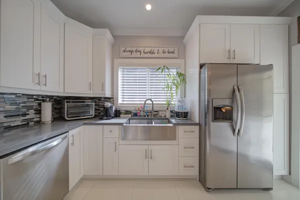 a large white kitchen with stainless steel appliances granite countertop a stove a sink a refrigerator and white cabinets with wooden floor