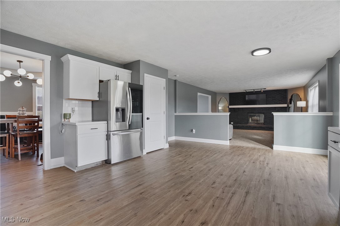 9278 Bryant Road Windham, OH 44288 - Photo 17 of 47 Kitchen featuring stainless steel refrigerator with ice dispenser, light wood-style floors, white cabinetry, a fireplace, and a textured ceiling